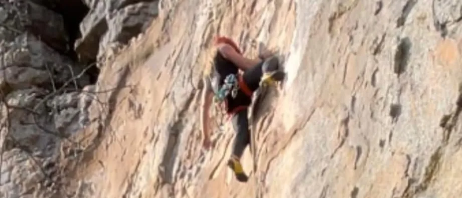 Cody Wood mid-move on a tan sandstone face, roped, red helmet